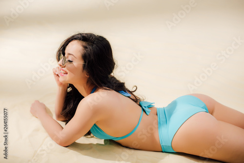beautiful sexy young woman in blue bikini and sunglasses lying on Beach