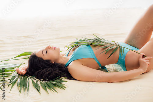 attractive sexy Young woman in bikini posing with green leaves while relaxing on beach