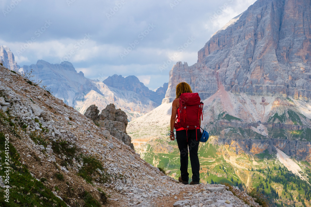 Young woman hiking in the Dolomites mountains, Italy, on Giro delle Cinque Torri, with storm clouds approaching. Guiding, touring in the mountains.