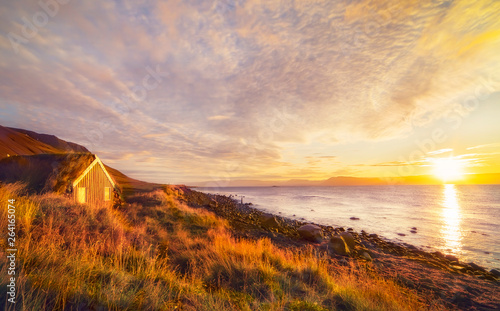 Dawn on the shore of the Atlantic Ocean. A traditional old house with a roof overgrown with grass on the beach. Iceland. Sea landscape. soft sunlight.