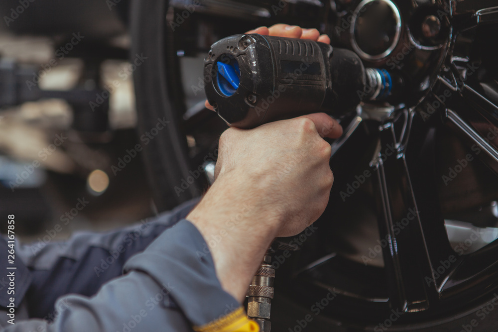 Cropped close up of a male mechanic in grey uniform torquing the lug nuts of a wheel with electric wrench Cropped close up of a male mechanic in grey uniform torquing the lug nuts of a wheel with electric wrench
