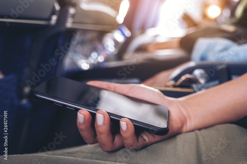 Closeup image of a woman holding a black smart phone while sitting in the cabin