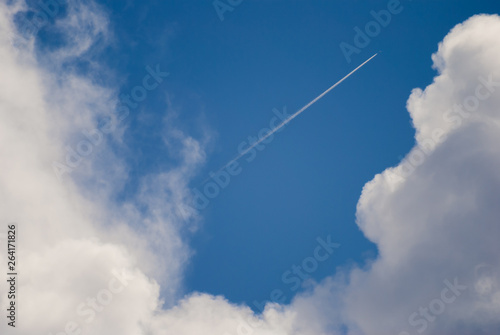 chem trails of plane flying far away on blue sky and clouds photo