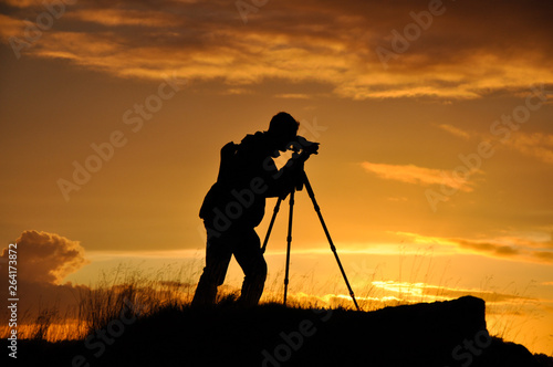 Silhouette of photographer with tripod against setting sun
