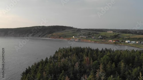 Cinematic drone / aerial footage rotating showing a few chalets and a forest by the sea in Kingsburg, Nova Scotia, Canada during summer season - sunset time. photo