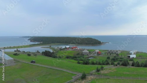 Cinematic drone / aerial footage rotating showing chalets and a car crossing a dirty road in the middle of a farm by the sea in Kingsburg, Nova Scotia, Canada during summer season photo