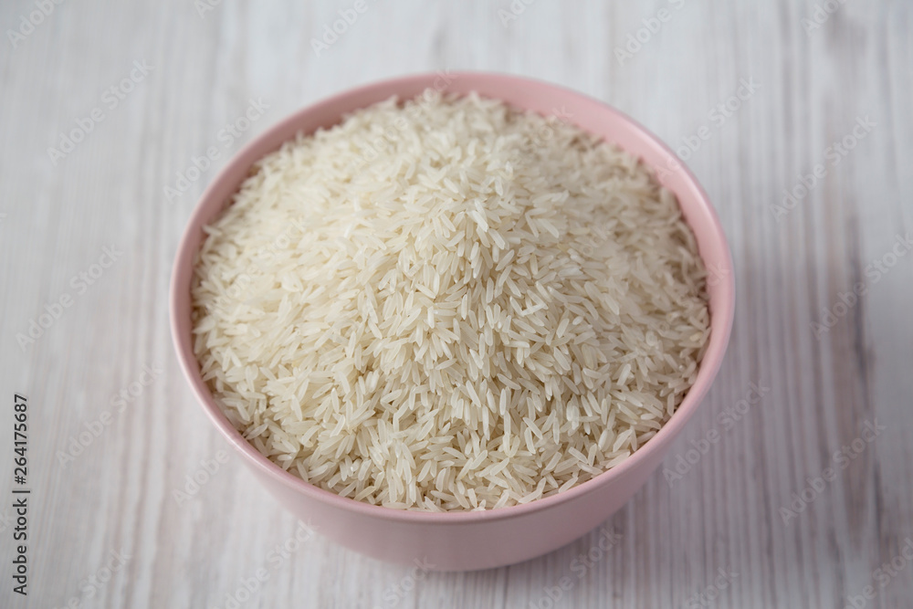 Dry white rice basmati in a pink bowl over white wooden background, side view. Close-up. Dry white rice basmati in a pink bowl over white wooden background, side view. Close-up.