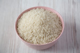 Dry white rice basmati in a pink bowl over white wooden background, side view. Close-up.