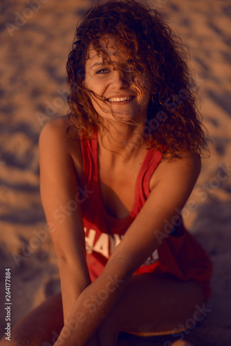 Slender young woman with curly hair and a bathing suit takes a breath in the evening on the beach in summer and smiling