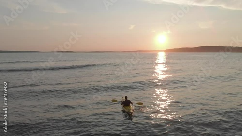 Cinematic drone / aerial static footage showing someone canoeing and another person surfing in the coast of Kingsburg, Nova Scotia, Canada during summer season - sunset time. photo