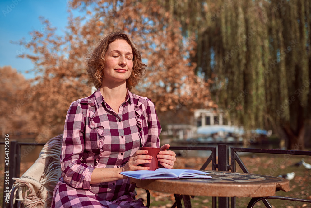 Pretty woman with mug and book in cafe in autumn park
Pretty woman with mug and book in cafe in autumn park