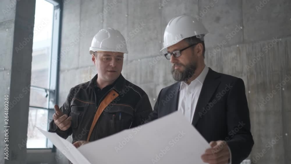 Two Caucasian Handsome Men In Helmets Talking And Looking At The Big Paper With. 4k Two Caucasian Handsome Men In Helmets Talking And Looking At The Big Paper With. 4k