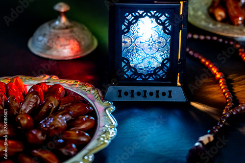 The Muslim feast of the holy month of Ramadan Kareem with dates on a tray on a dark background. Beautiful background with a shining lantern Fanus.