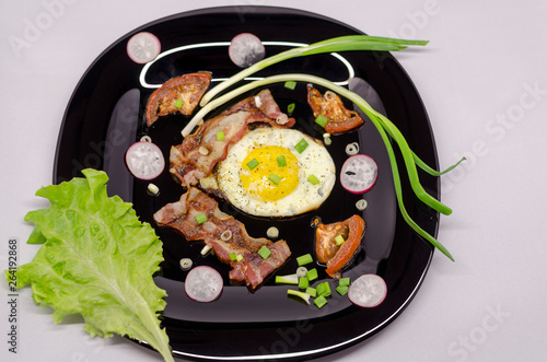 fried eggs on a black dish decorated with green vegetables, tomatoes and spices