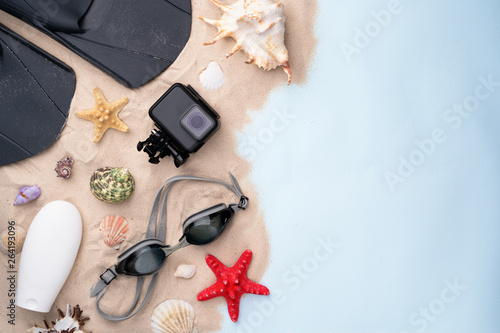 Swimming goggles, flippers, sunscreen and action camera on the sand with shells and starfishes.