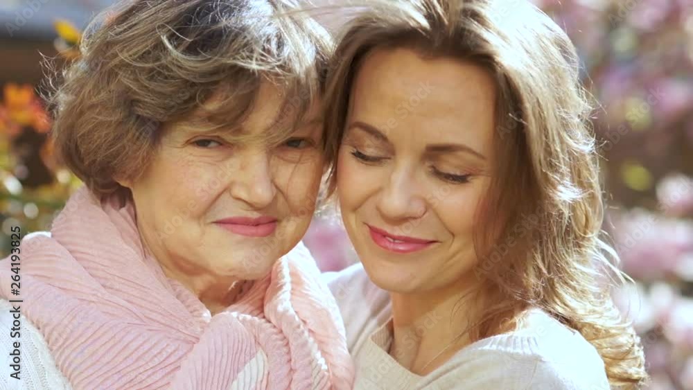 Mother and daughter, close spring portrait in the blooming garden. Women laugh, hug and kiss each other Mother and daughter, close spring portrait in the blooming garden. Women laugh, hug and kiss each other