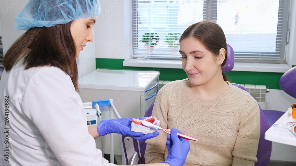 Woman dentist showing to patient on a jaw model how to clean the teeth with toothbrush properly Woman dentist showing to patient on a jaw model how to clean the teeth with toothbrush properly