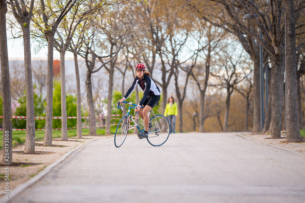 Young handsome male cyclist in sportswear and protective helmet cycling bike on road in park