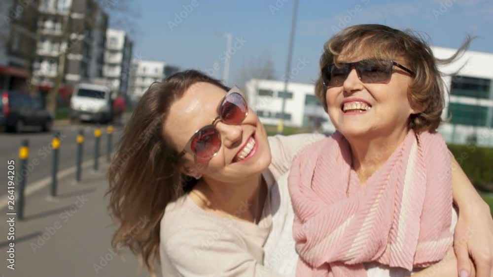 Two women, portrait close, mother and daughter on a city street. Sunny day, women with glasses are laughing and hugging Two women, portrait close, mother and daughter on a city street. Sunny day, women with glasses are laughing and hugging