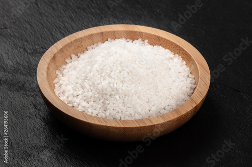 A closeup photo of a bowl of sea salt on a black slate background