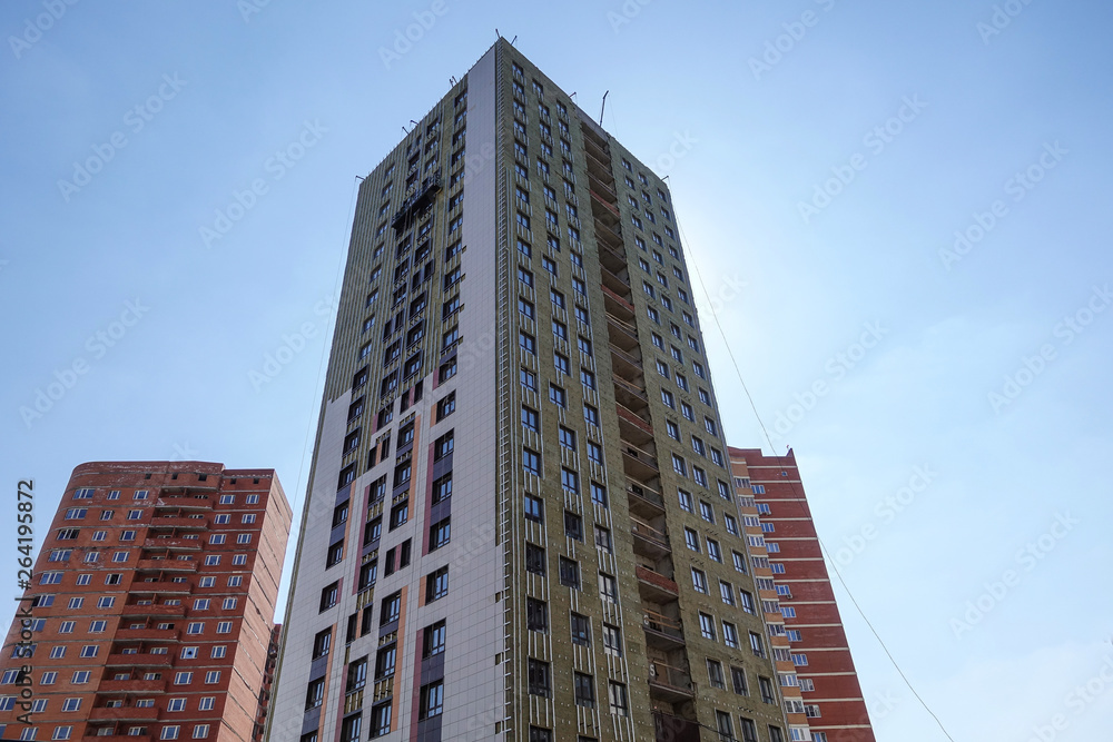 High-rise building under construction against the blue sky. The building is trimmed with external decorative panels. Russia