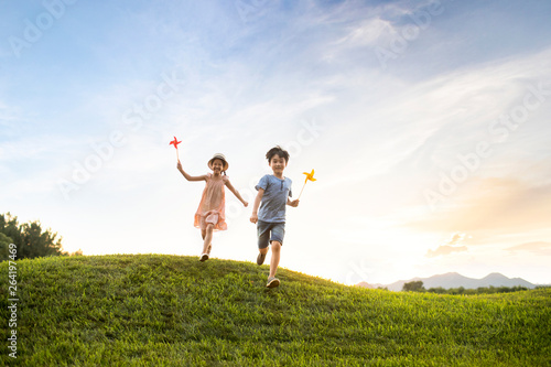 Two children playing paper windmill on meadow