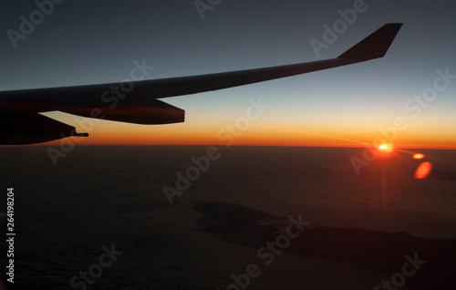 Panorámica con ala de avión y puesta de sol sobrevolando una isla