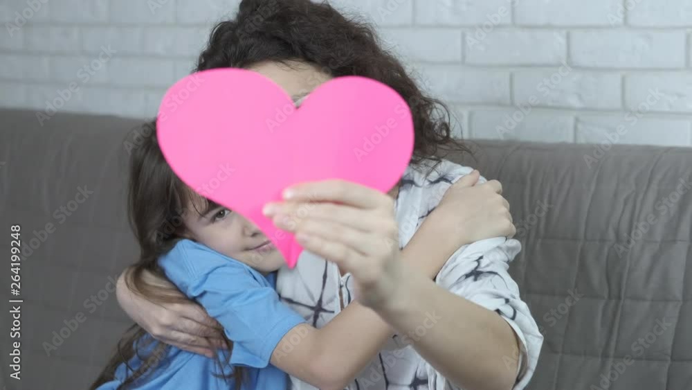 Mother and daughter love. A happy mother and daughter sit embracing with a paper heart in their hands. Mother and daughter love. A happy mother and daughter sit embracing with a paper heart in their hands.