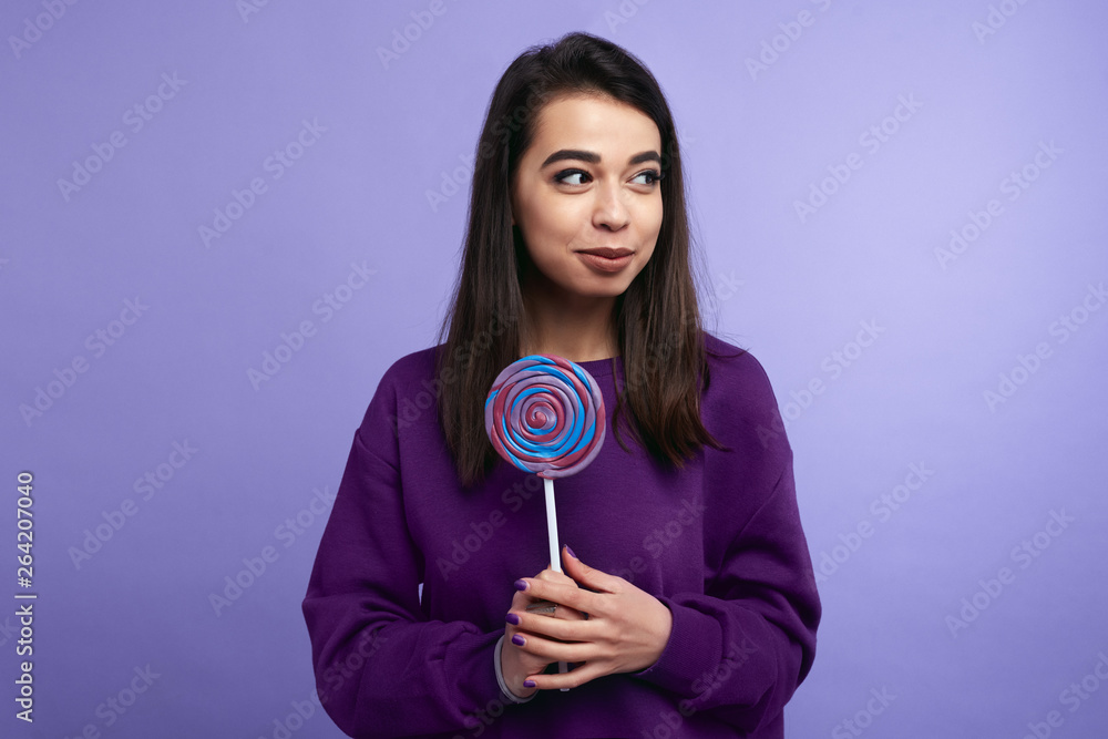 Portrait of happy young female holding a purple lollipop isolated over violet background Portrait of happy young female holding a purple lollipop isolated over violet background