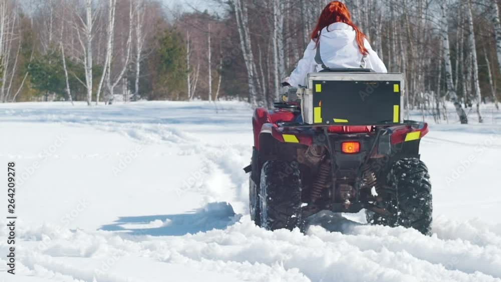 A winter forest. A woman with ginger hair riding snowmobile and overcoming the snow A winter forest. A woman with ginger hair riding snowmobile and overcoming the snow