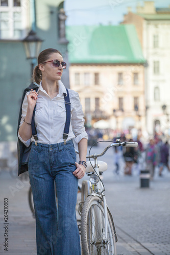 Woman in jacket and jeans walking on the street. Cheerful stylish woman with sunglasses outdoor. Woman wearing shades while looking away in the city street