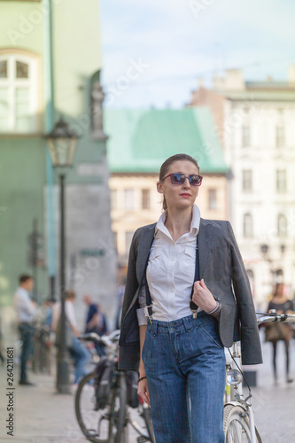 Woman in jacket and jeans walking on the street. Cheerful stylish woman with sunglasses outdoor. Woman wearing shades while looking away in the city street © Serg