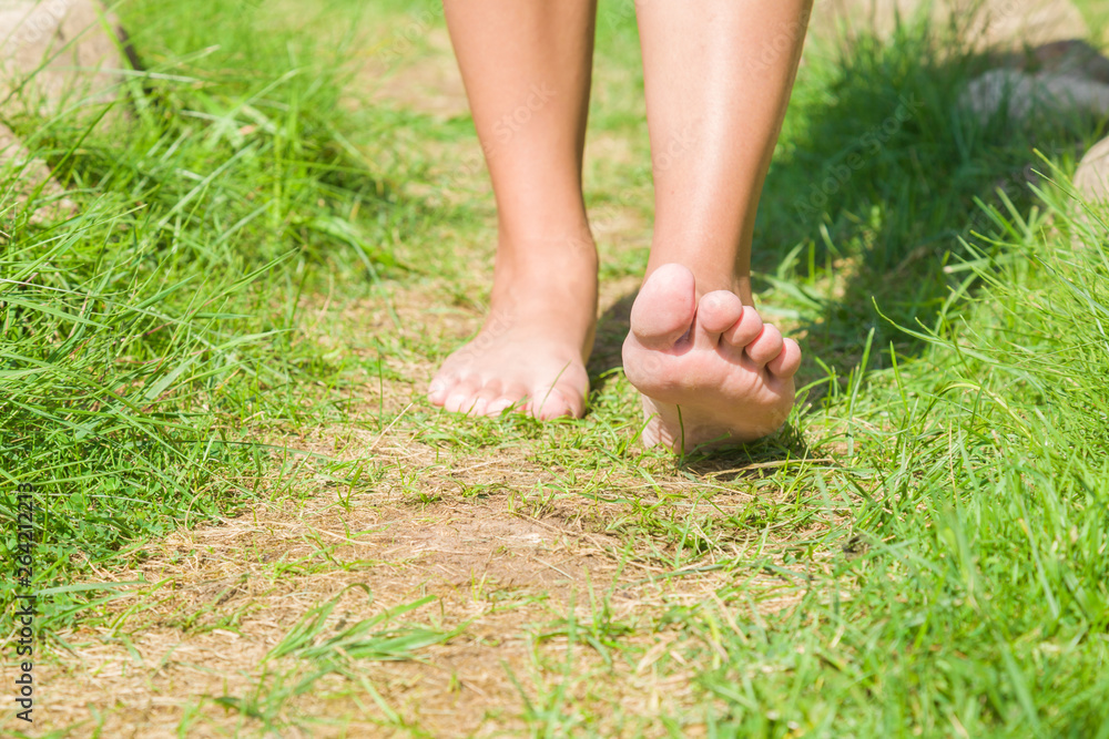 Young woman barefoot walking on natural trail in sunny summer day. Fresh, green grass. Healthy lifestyle. Bright color. Closeup. Low angle. Front view.