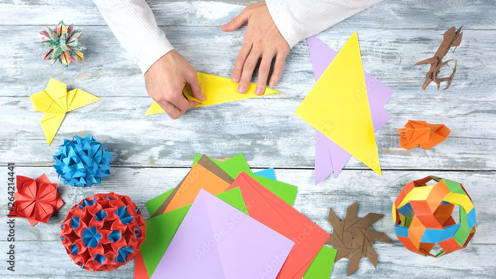 Fototapeta premium Torning yellow paper by hands. Folding colorful paper while making origami figures. Top view, flat lay.