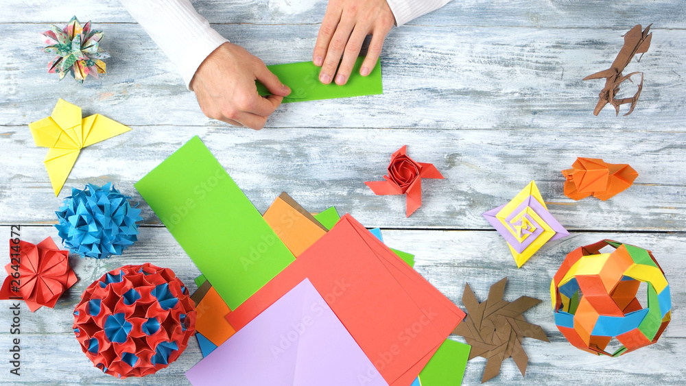 Fototapeta premium Hands making origami with green paper. Person folding green paper sheet. Origami exhibition project.