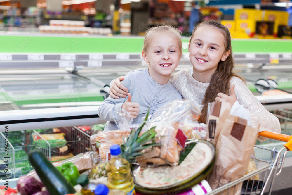 Two girls are standing with cart with products in the supermarket.