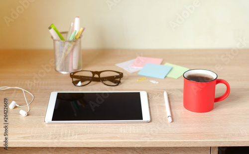 Wooden Desk. White tablet with black-rimmed glasses. Cup of tea.