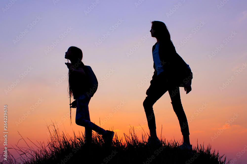 People, Teens, Friendship, Family, Hiking And Travel Concept. Silhouette Of A Young Girls On A Mountain Top.Young Girls With Backpack Enjoying Sunset. Female Friends Playing Outdoors.