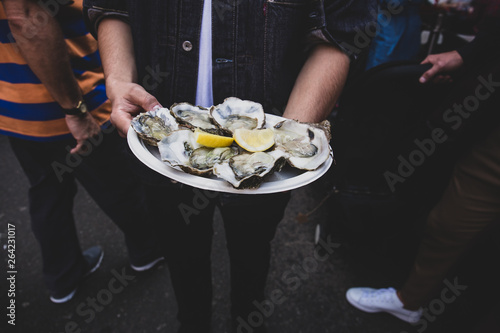 Obraz na plátně Man hand holding fresh raw oyster in paperr plate with lemon in market