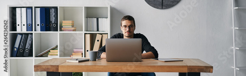Young man working with computer, phone and tablet at the table while drinking coffee