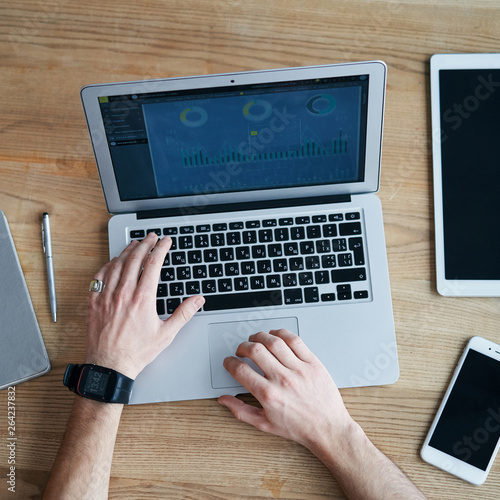 View from the top, hands working with laptop and smartphone on wooden table