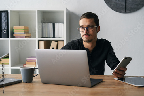 Young man working with phone and computer, receiving phone call, talking with partners 