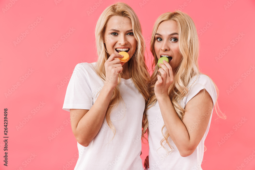 Happy blonde twins wearing in t-shirts eating cakes Happy blonde twins wearing in t-shirts eating cakes