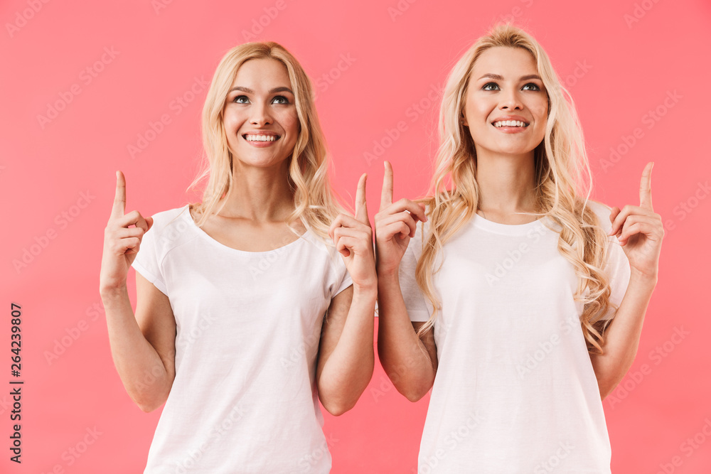 Smiling twins wearing in t-shirts pointing and looking up Smiling twins wearing in t-shirts pointing and looking up