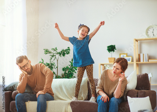 naughty, mischievous, child girl jumping, laughing and having fun, parents stressed with headache.