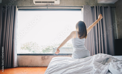 Back view of young healthy woman stretching in bed after her waking up in the morning, start a new day with happiness. 