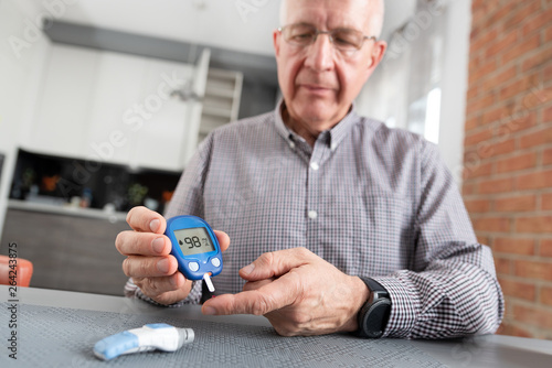 Senior man checking blood sugar level at home photo