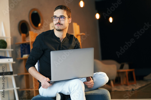 Young man sitting with computer. Freelancer in glasses working with laptop, project manager.
