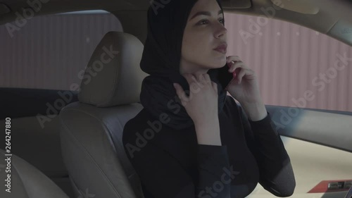 Portrait of independent young muslim woman sitting in her car lookiing to herself in mirrir and talking by the smartphone photo