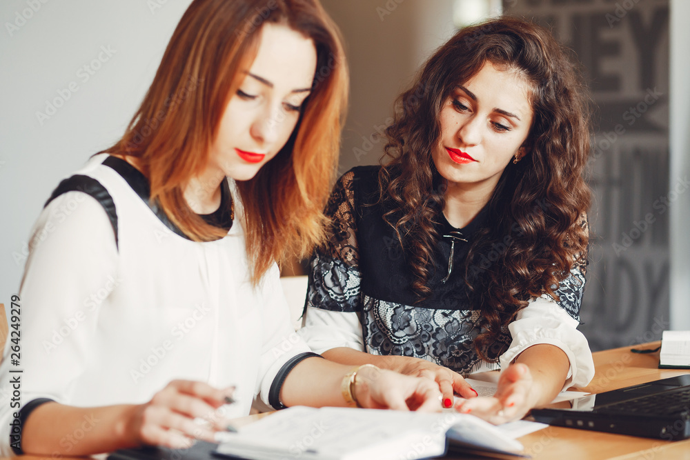 Girls are sitting at the table.Beautiful girls work in the office. Women with a computer Girls are sitting at the table.Beautiful girls work in the office. Women with a computer